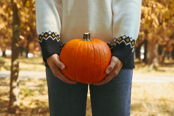 Woman in sweater and jeans hold pumpkin outdoor