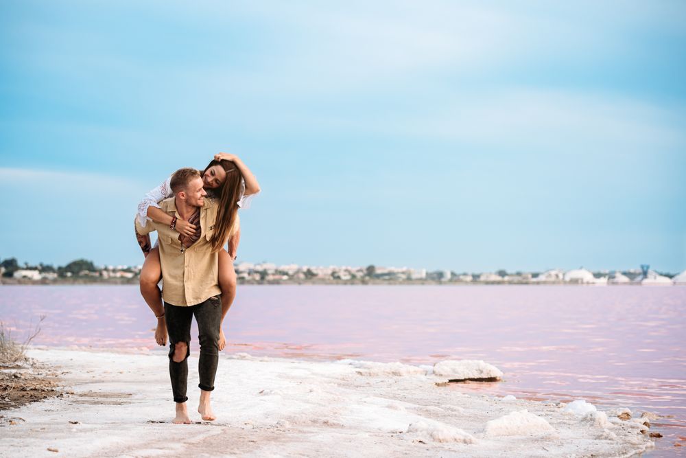 adorable couple giving a piggyback ride on an amazing beach of pink water