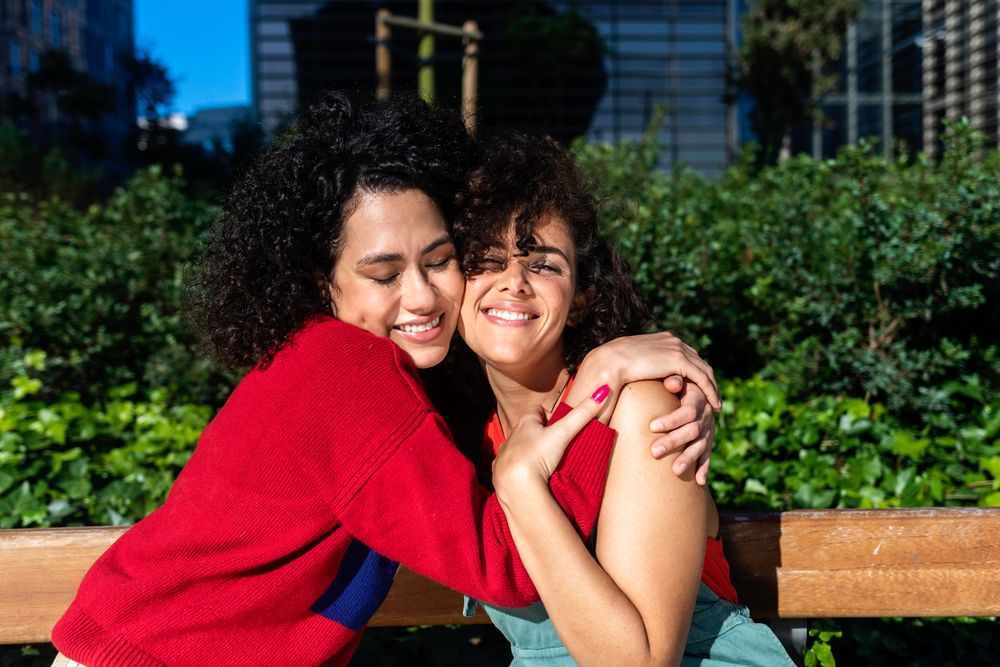 Female couple smiling while in love hugging in city park