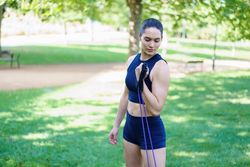 A woman exercises with resistance bands in a park, showing determination and focus on her outdoor workout