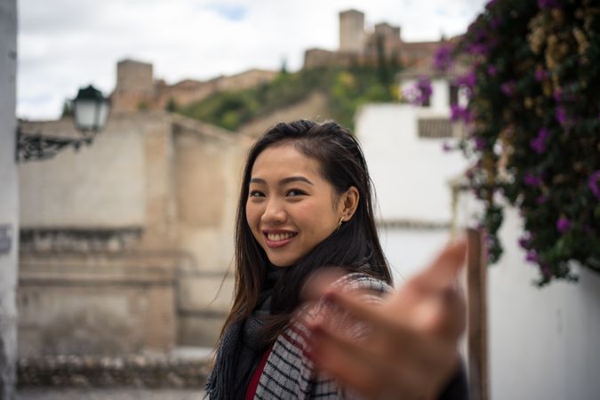 Asian female traveler in warm wear smiling among old buildings near big castle