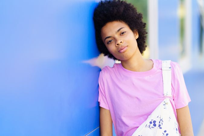 Serious woman looking at camera and leaning her side on blue building