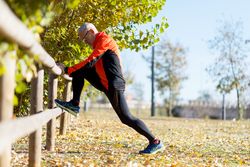 Side view of male stretching legs on wooden fence