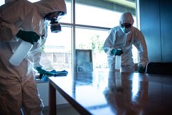 Two men in PPEs sanitizing table in meeting room during lockdown in Milano, Italy 