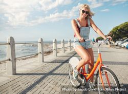 Stylish young female cycling on a seaside promenade on a summer day 412Xjb