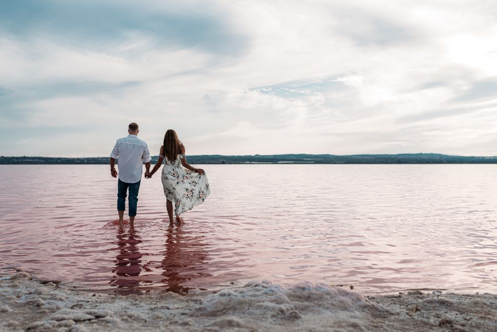 back view of adorable couple walking into an amazing beach with pink water