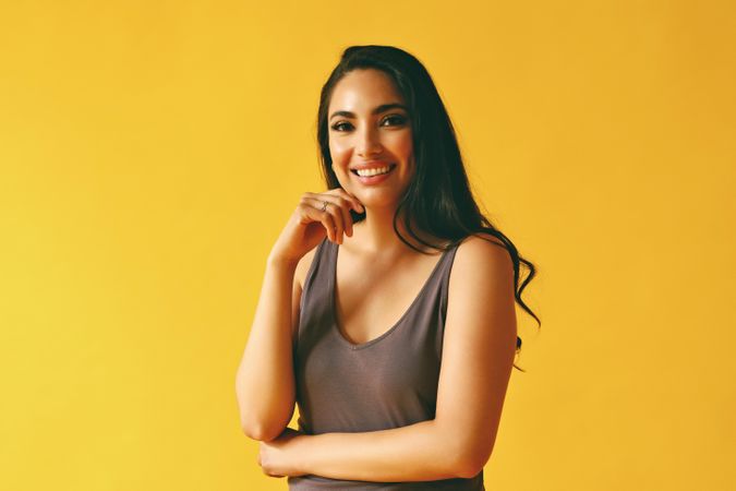Happy Hispanic woman standing and looking at camera in yellow room, copy space