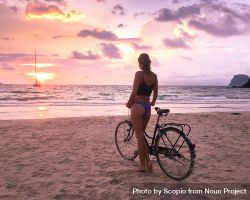 Woman wearing biking standing beside bicycle on the beach at sunset 41AXj4