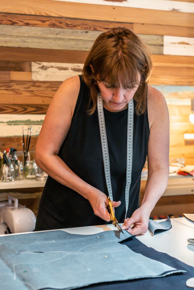 Seamstress using scissors to cut textile at work table. Vertical Shot