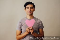 Romantic Hispanic male holding cut out pink heart to his chest 5naM80
