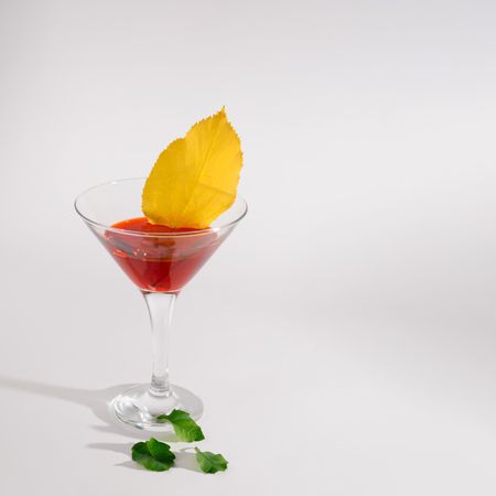Red cocktail garnished with yellow fall leaf