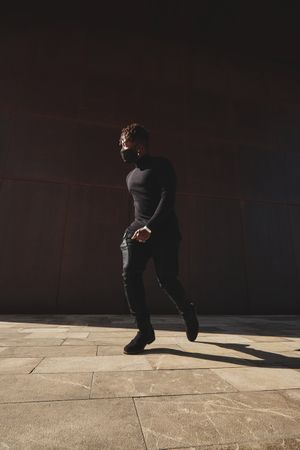 Stylish Black man walking on pavement in dark clothes