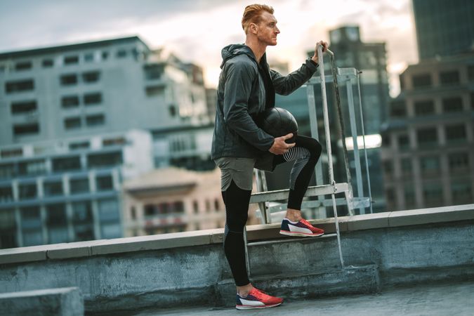 Athlete standing near a rooftop staircase with a medicine ball in hand