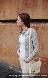 Woman wearing gray jacket, pink jeans and satchel bag over a stone wall background 4d8eJE