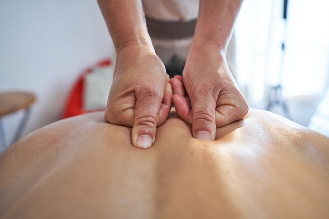 Faceless masseuse massaging back of client