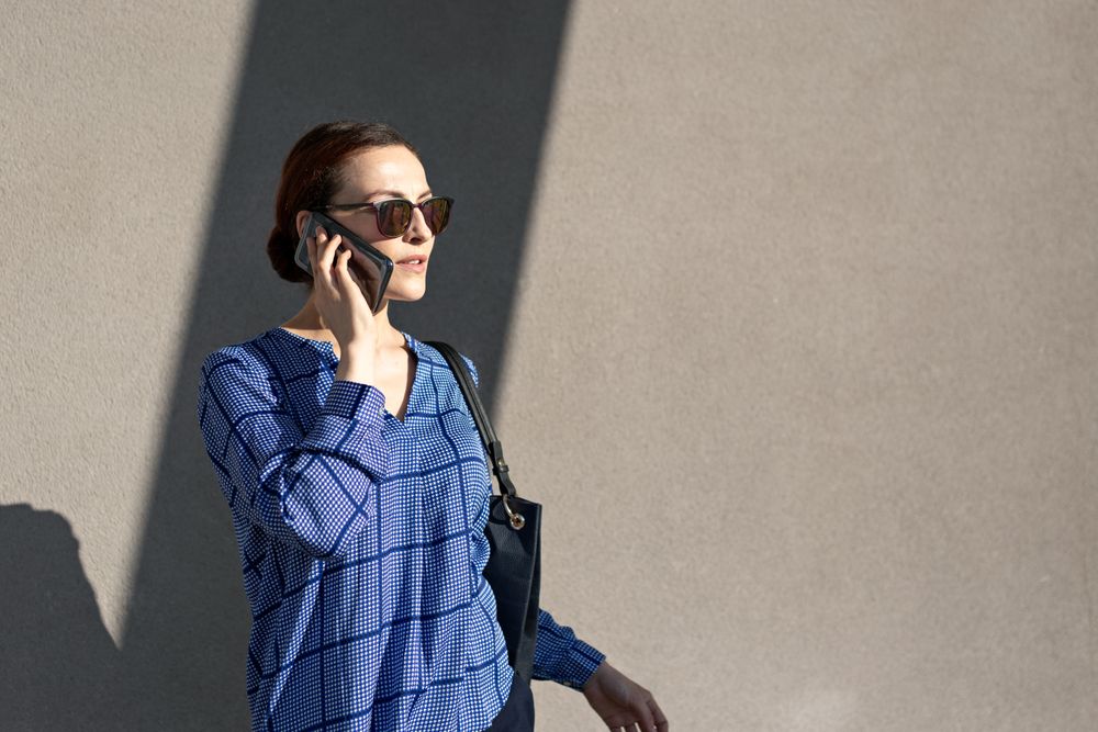 Businesswoman having smartphone conversation near gray wall