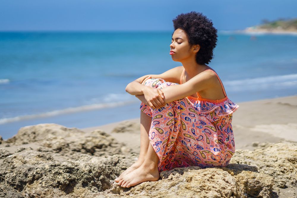 Woman with eyes closed sitting on the rocks on the coast by the sea