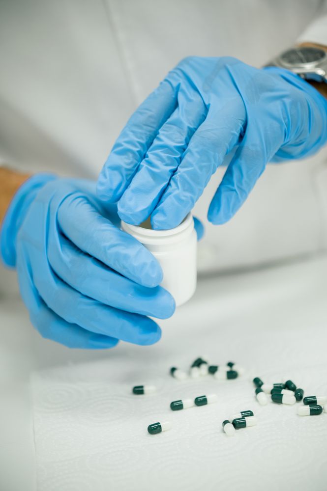 Crop pharmacist in gloves putting capsules into bottle