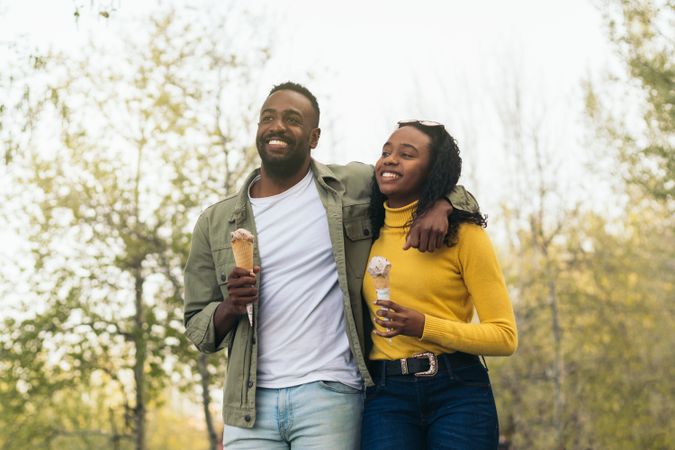 Black couple eating ice cream while walking in a park
