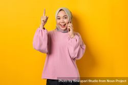 Excited Muslim woman on the phone and pointing upwards with good idea 438Xgb