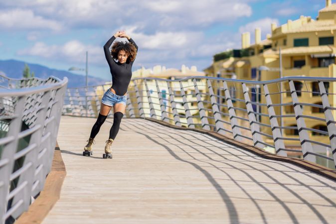Happy woman with afro hairstyle rollerblading on wooden bridge