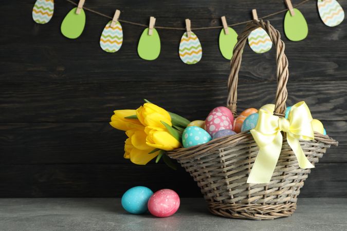 Easter basket filled with colorful eggs and flowers on a wooden background