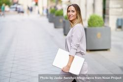 Content woman in grey walking outside with laptop 5qk1Da