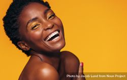Close up of young woman with makeup laughing against yellow background 5qDqp0