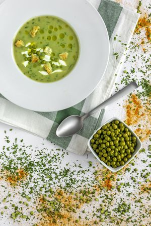 Green vegetable cream soup with crackers and peas in bowl