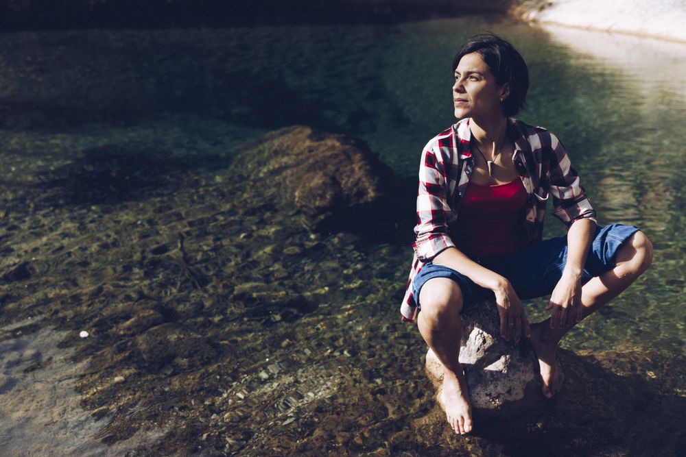 Cheerful woman sitting on rock in clear water