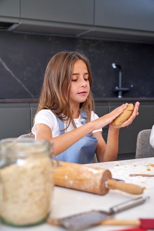 Serious cute kid making dough at table in kitchen