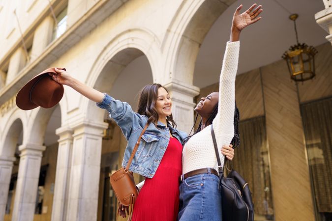 Female friends embracing each other with their arms up on an outdoor street