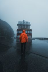 Back view of person in orange jacket standing facing a store under rainy weather