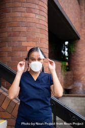 Woman nurse standing outside putting on face shield 49mam4