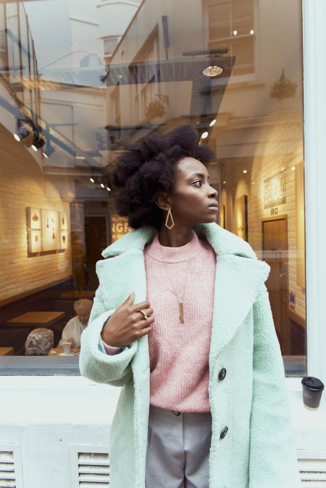 Woman in turquoise coat standing on sidewalk looking away