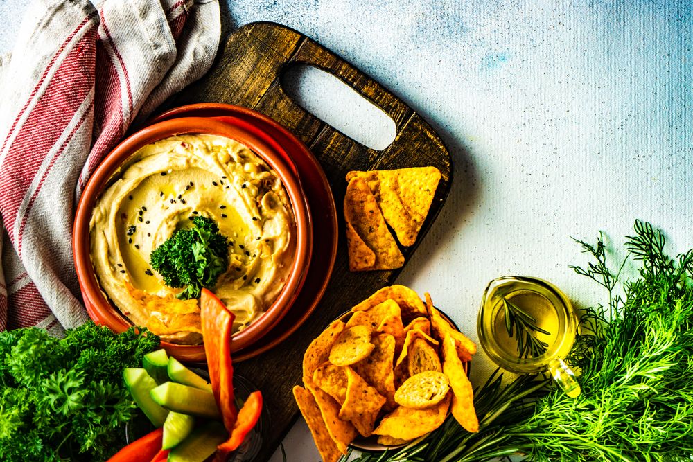 Top view of creamy hummus dip with chips and vegges on bread board