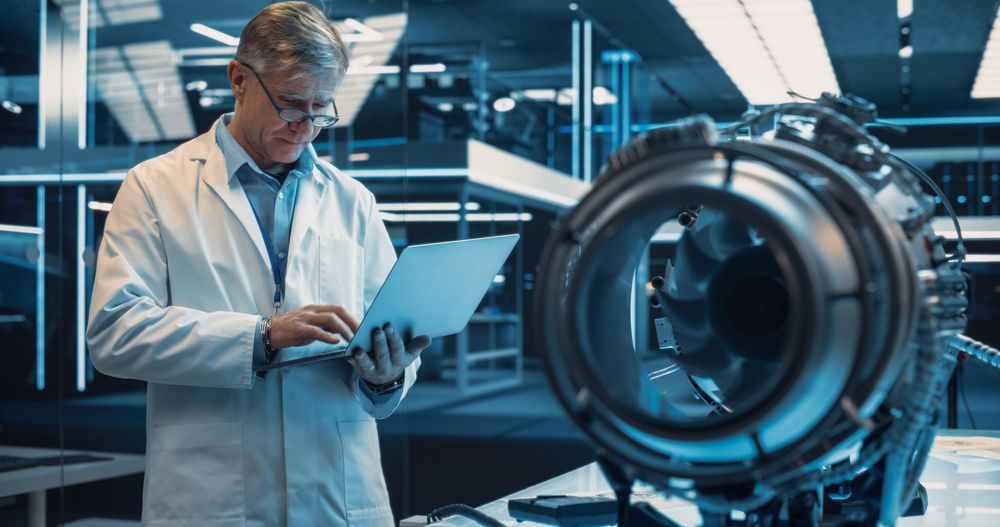 Professional Adult Engineer Using a Laptop Computer, Analyzing and Checking How a Modern Electric Turbine Motor Works.