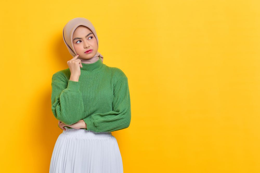 Woman in headscarf pondering something with hand on her cheek with copy space