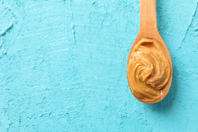 Spoon with peanut butter on color background, space for text and top view