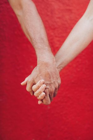 Close up of couple holding hands against red wall