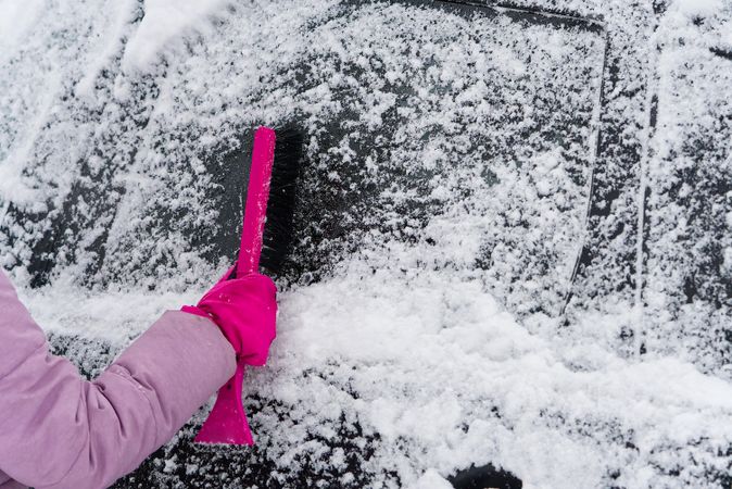 Person brushing off snow from car windshield