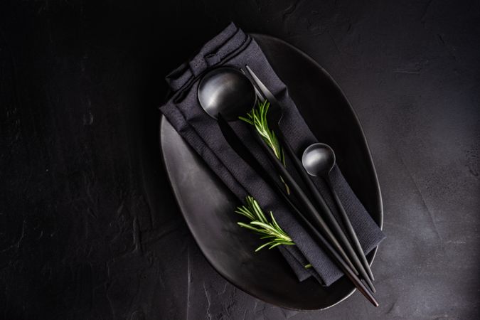 Sleek table setting in dark color with rosemary sprig and copy space