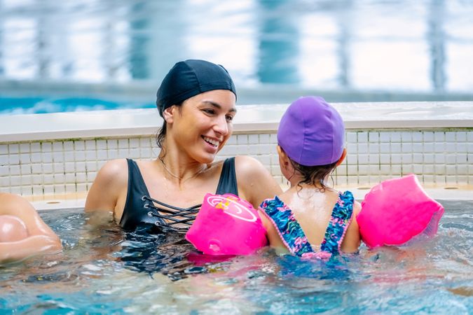Cheerful girl swimming in pool with mother