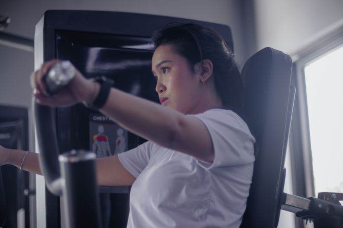 Determined young woman using chest press machine in modern gym