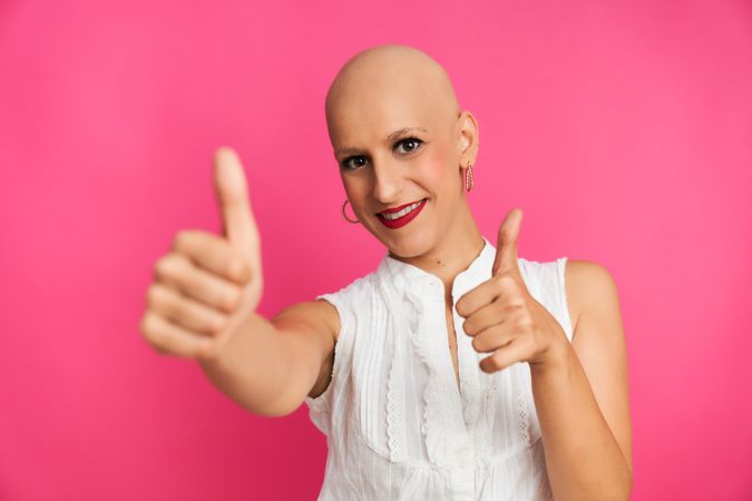 optimistic woman suffering from cancer with shaved head and positive gesture on pink background