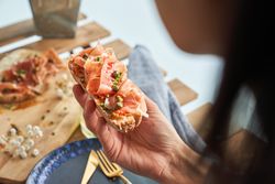Crop woman enjoying delicious toast with prosciutto on terrace