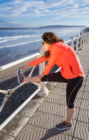 Athletic woman warming up before running on the beach promenade on a summer morning