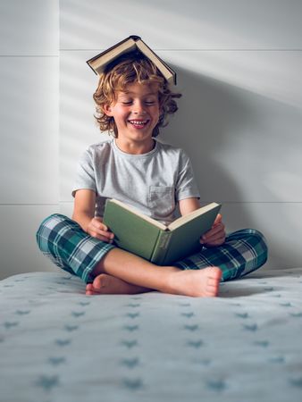 Cheerful preschool boy reading book on bed