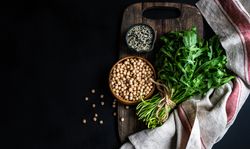 Top view of bowl of garbanzo beans and sesame seeds next to arugula 