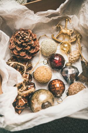 Wooden box of rustic holiday tree decorations, pine cones, balls, laying on tissue paper, close up